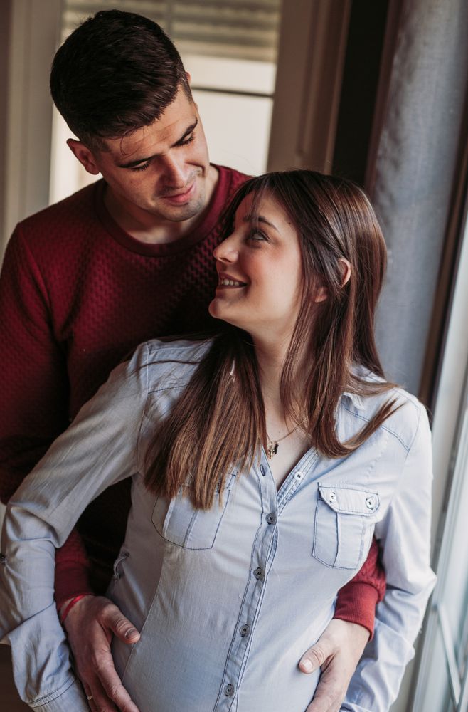 Pregnant woman with husband looking at window at home