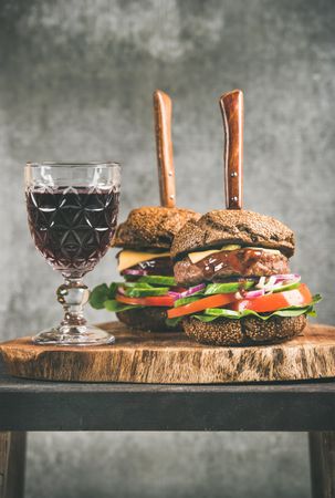 Two cheeseburgers skewered with knives, with fresh vegetables and wine, vertical composition