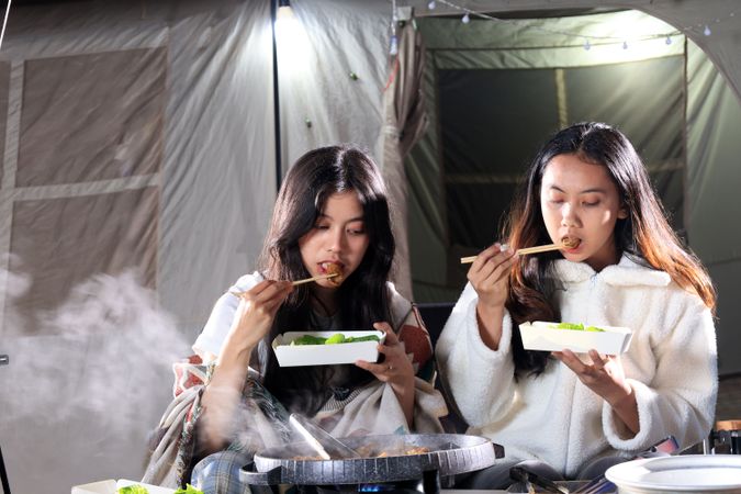Two Female Asian  Friends Eat  Barbeque  Meat in front of Camping Tent
