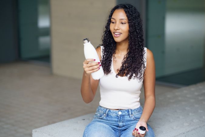 A Young Woman is Sitting Outdoors While Enjoying a Refreshing Drink and Smiling Happily