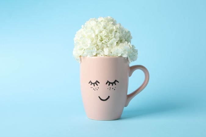 Cup with hydrangea flowers on blue background. Spring plant
