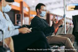 Man in face mask sitting at airport terminal and video calling 42Py10