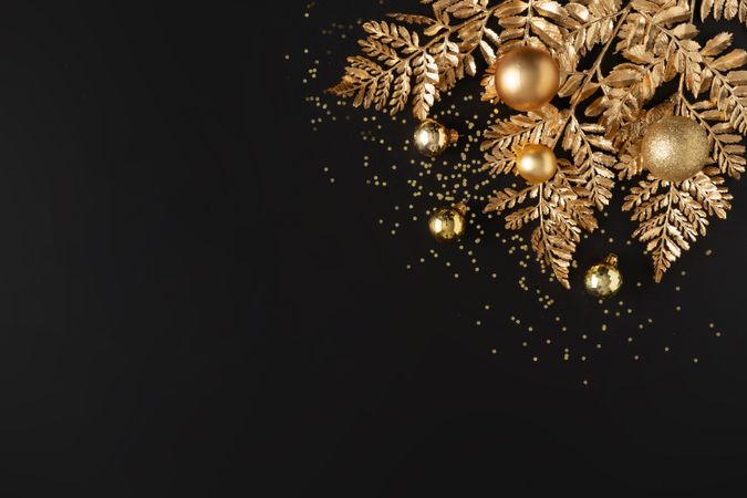 Golden holiday decorations, glitter, baubles and leaves on dark background