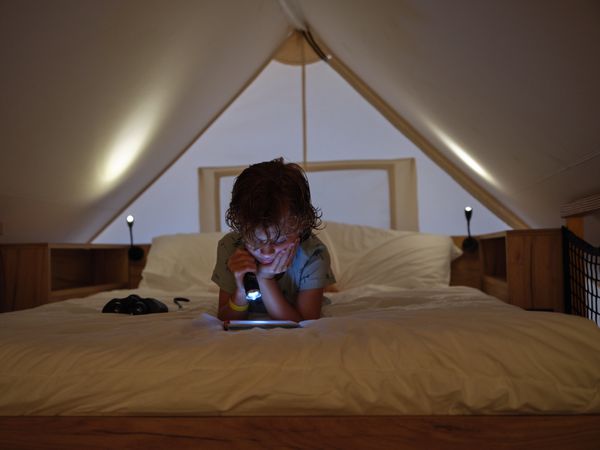 Focused boy reading book with flashlight on bed