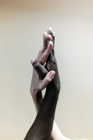 Black hand and white hand touching against light background
