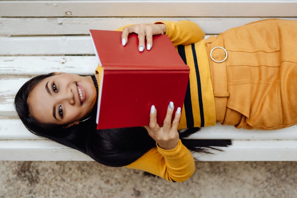 Graceful long haired Asian woman reading book on bench in park
