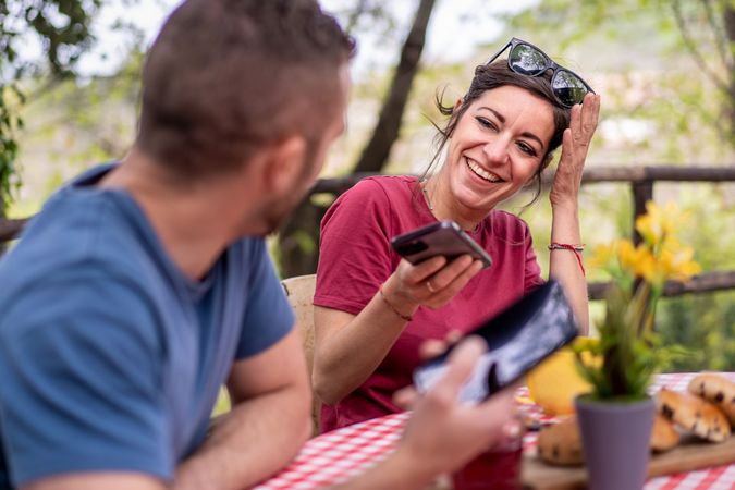 Woman laughing joyfully as she shares content on her smartphone with a friend during an outdoor gathering
