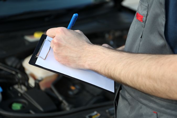 A man in overalls writes to a clipboard. Mechanic. Car inspection