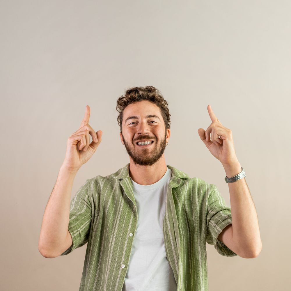 Happy young man pointing up with both fingers on a neutral background.