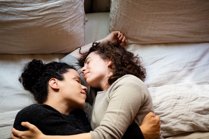 Two women lying down on bed sleeping in loving embrace