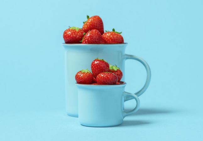 Fresh strawberries in cups on a blue colored table