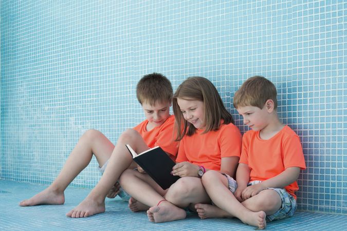 Children sitting in empty pool and reading book