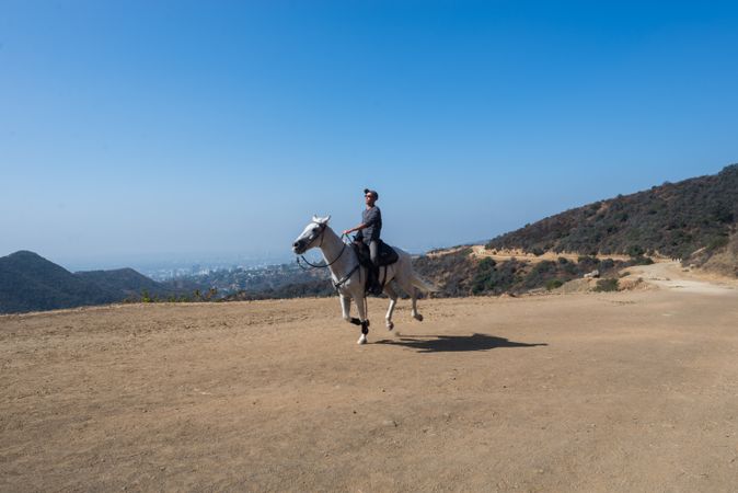 Man riding a horse on dirt trail with blue sky behind