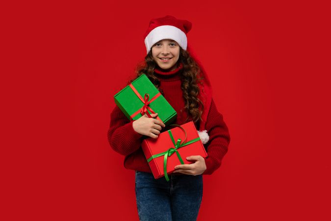 Happy girl in Santa hat holds multiple Christmas presents.