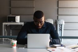 Black guy video chatting on tablet near laptop in workplace