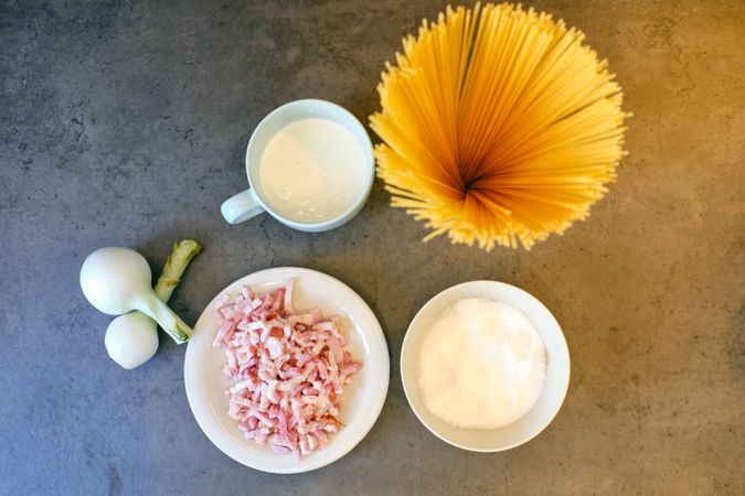 Raw spaghetti with bacon slices and milk cream in cup