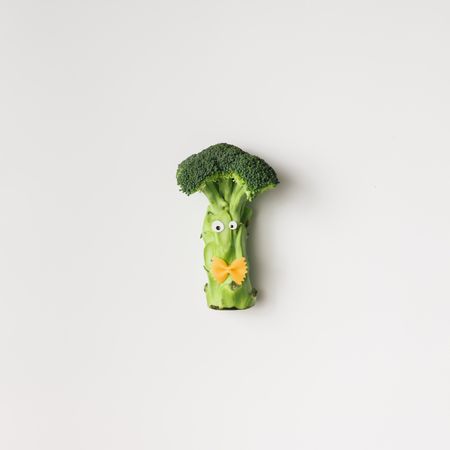 Broccoli with googly eyes and bowtie pasta on light background