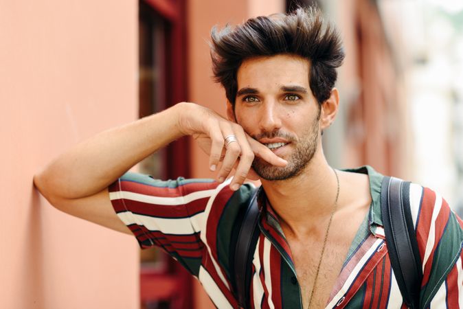 Attractive man with dark hair standing outside looking in the distance with hand to his face