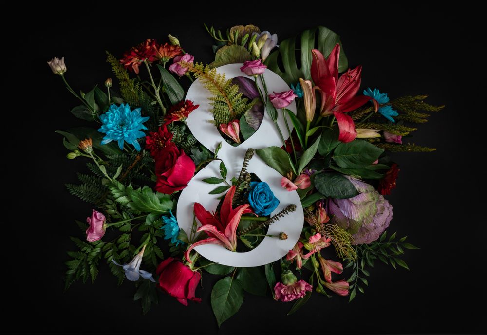 Colorful spring flowers of red, blue, pink, cream around the number “8” on dark background