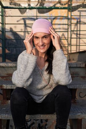 Smiling woman adjusting pink headscarf on stairs