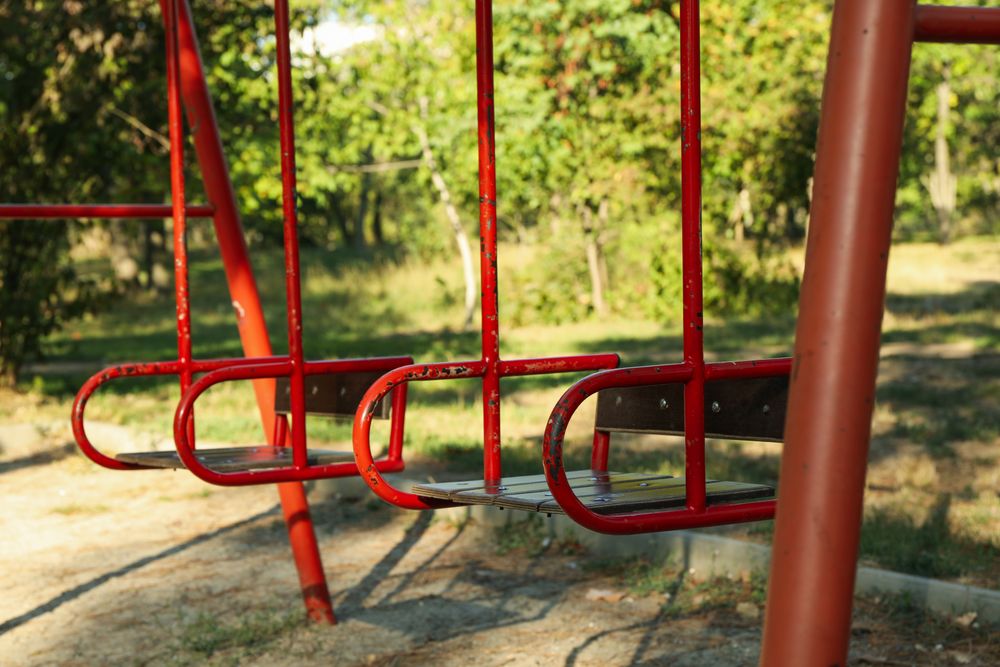 Red swings in city park in bright sunny morning