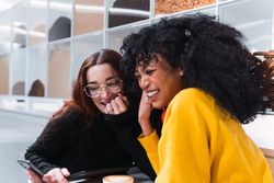Positive multiethnic female friends using smartphones and laughing in cafe