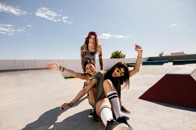 Two women sitting on skateboard being pushed by a friend