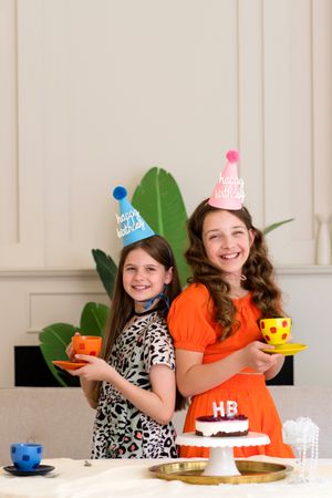 Two girls standing back-to-back in birthday hats