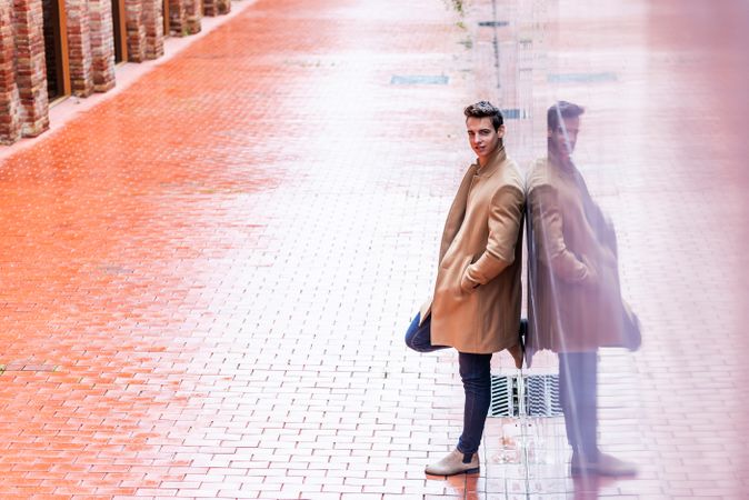 Side view of man leaning on reflective wall outside in autumn coat