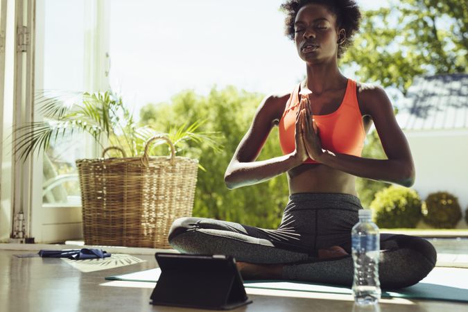 Focused woman meditating at home using a tablet for workout