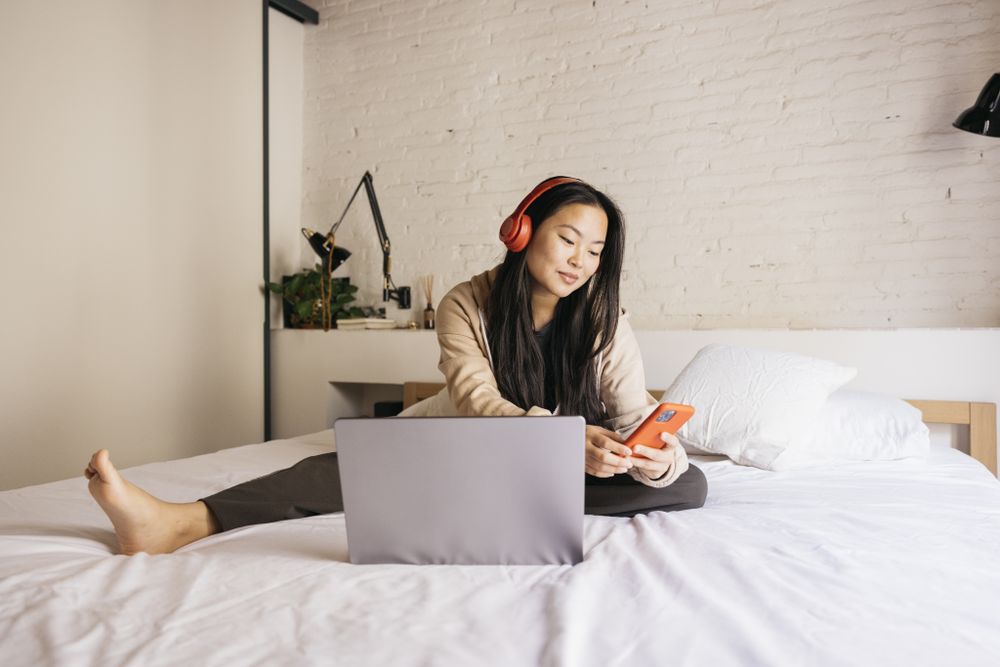 Young female using laptop and phone on bed