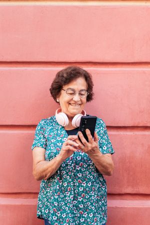 Older woman using smartphone and listening to music with headphones