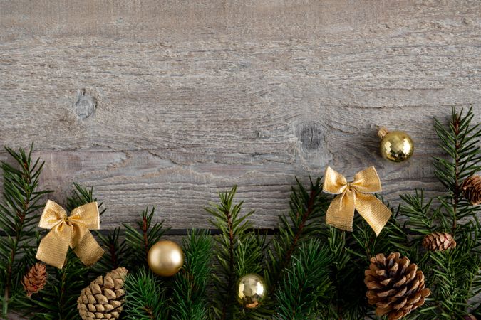 Pine branches bordering bottom of wooden background with gold ribbons