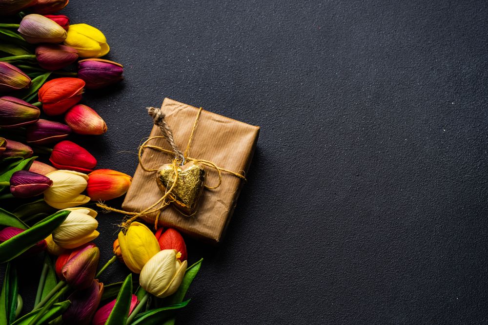 Fresh tulips and brown wrapped present on dark table with copy space