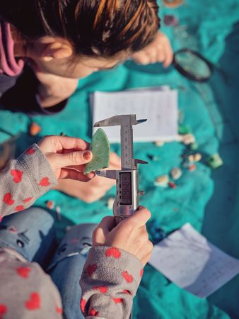 Crop girl putting piece of plastic into digital caliper