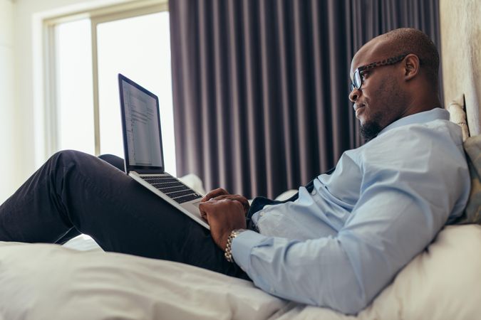 Man in a suit working on laptop while lying in bed