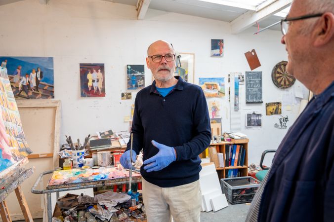 Older male artist talking with male friend in studio