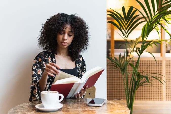 Black woman reading book at cafe table