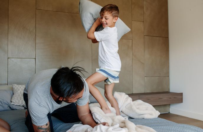 Man and boy playing with pillows on bed