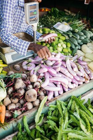 Vendor with fresh vegetables for sale displayed at Sri Lankan market, vertical