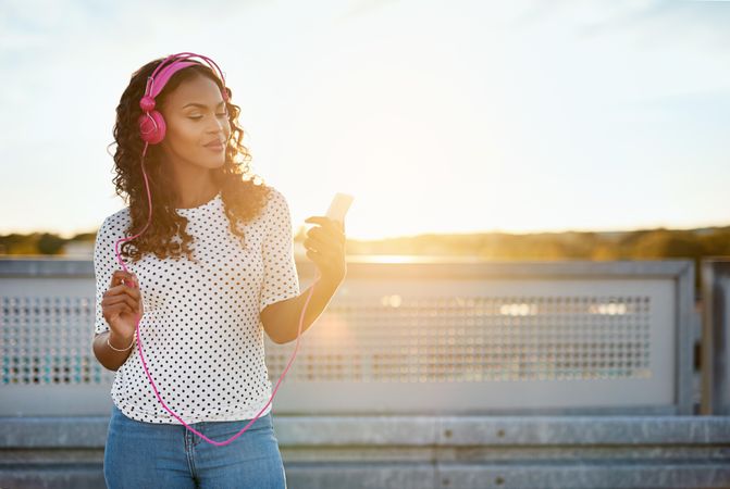 Woman on sunny roof top wearing pink headphones on