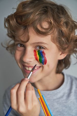 Smiling boy painting rainbow on face