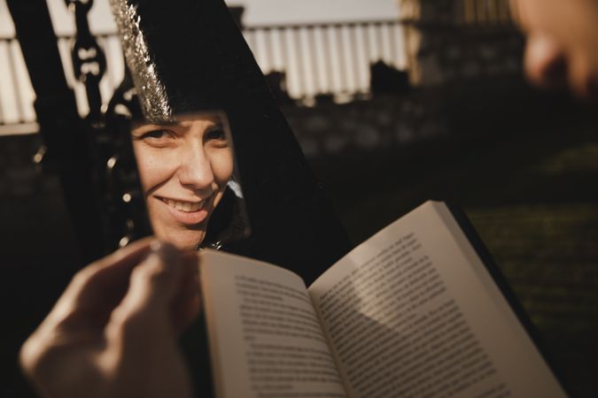 Reflection of smiling woman with book near fence