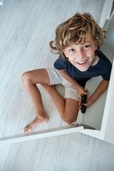 Cheerful boy sitting on floor with screwdriver