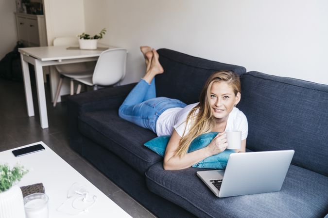 Woman lying on sofa with laptop computer working remotely from home
