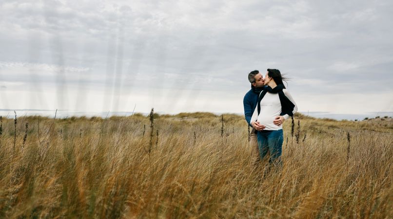 Pregnant woman with partner kissing and holding belly