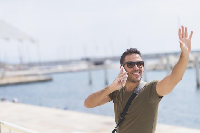 Male with arm up greeting friends in distance while talking on cellphone