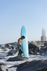 Male surfer with blue board standing in the sea around a rocky beach