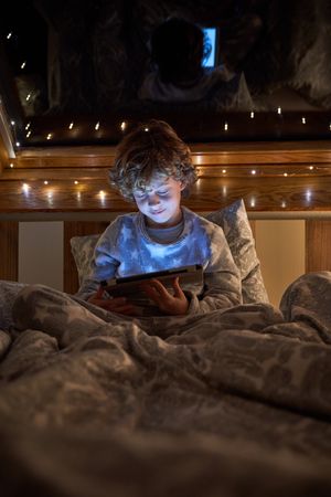 Boy playing game on tablet in dark bedroom