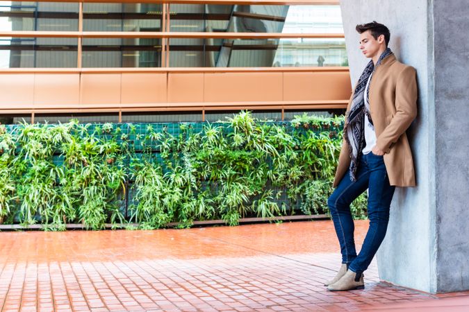 Serious man in camel coat looking away leaning on wall outside